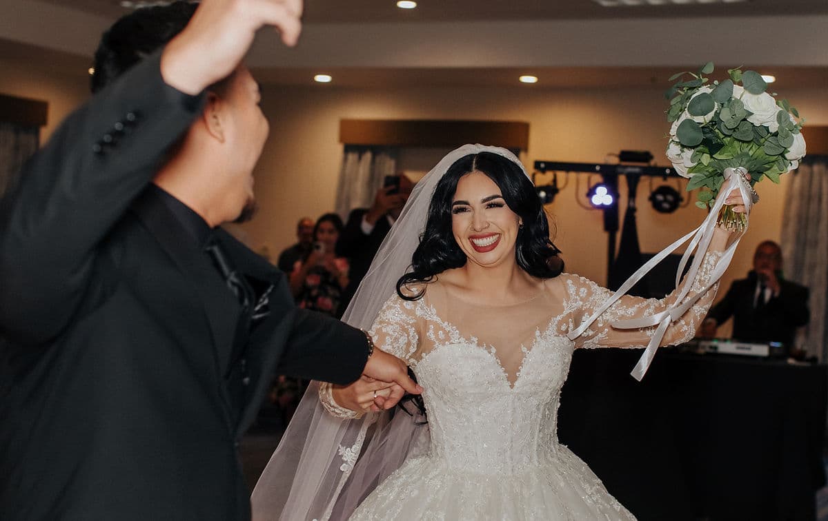Bride laughing on the dance floor with her bouquet raised