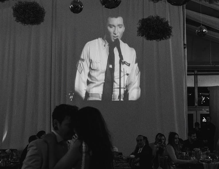 Couple dancing while a classic film plays on a projection screen behind them, black and white