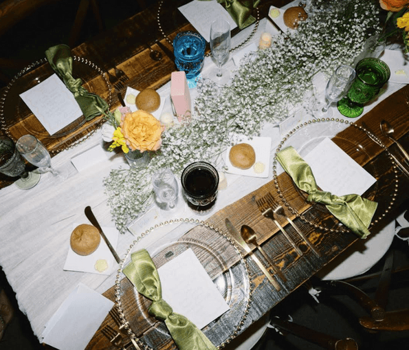 Overhead view of a wooden reception table with a baby's breath runner, green silk napkins and beaded charger plates
