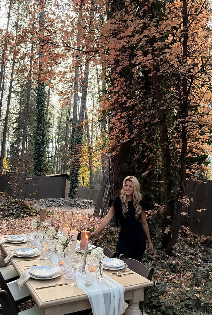 Arabella in a black dress standing at a candlelit forest tablescape