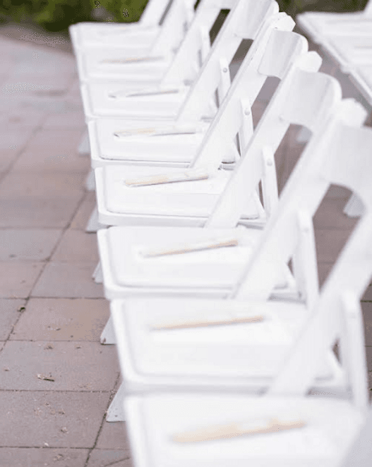 Rows of white folding ceremony chairs on a paved terrace