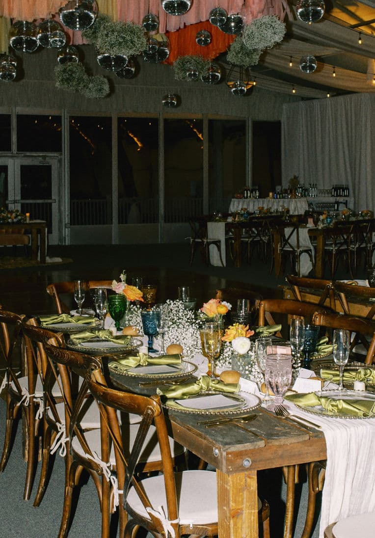 Reception tent with cross-back chairs, green silk napkins, disco balls and baby's breath