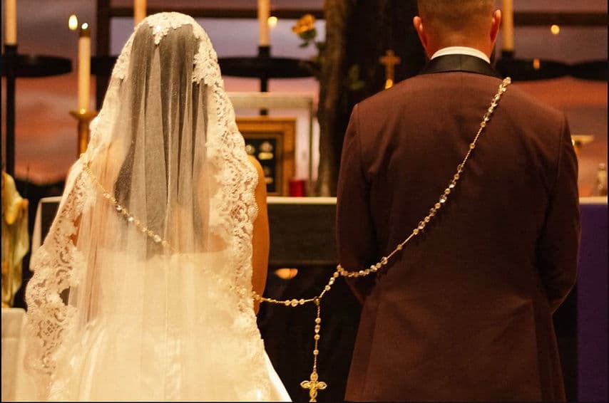 Bride and groom at the altar joined by a wedding lasso rosary