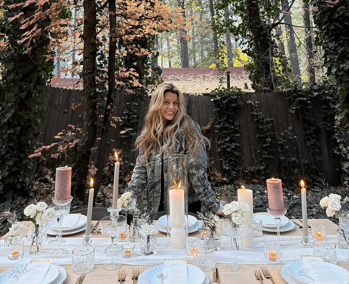 Arabella smiling behind a fully set candlelit table in a forest backyard