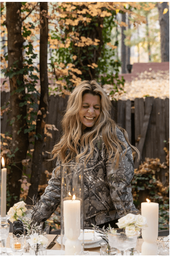 Arabella laughing behind a candle-lit tablescape of white florals and autumn foliage