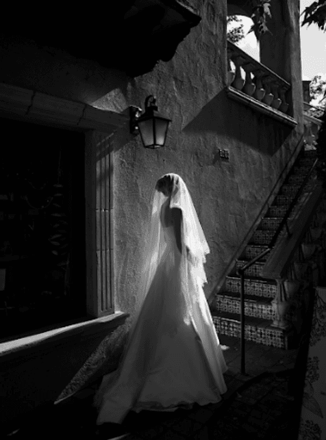 Bride in a long veil standing beneath a lantern beside a tiled staircase, black and white
