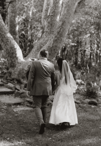 Bride and groom walking hand in hand up a wooded path, black and white