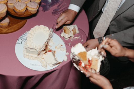 Cutting a white buttercream wedding cake beside a tray of cupcakes