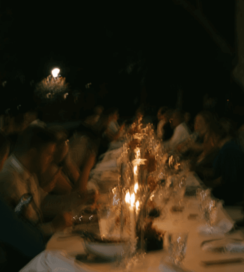 Guests dining at a long candlelit table outdoors at night