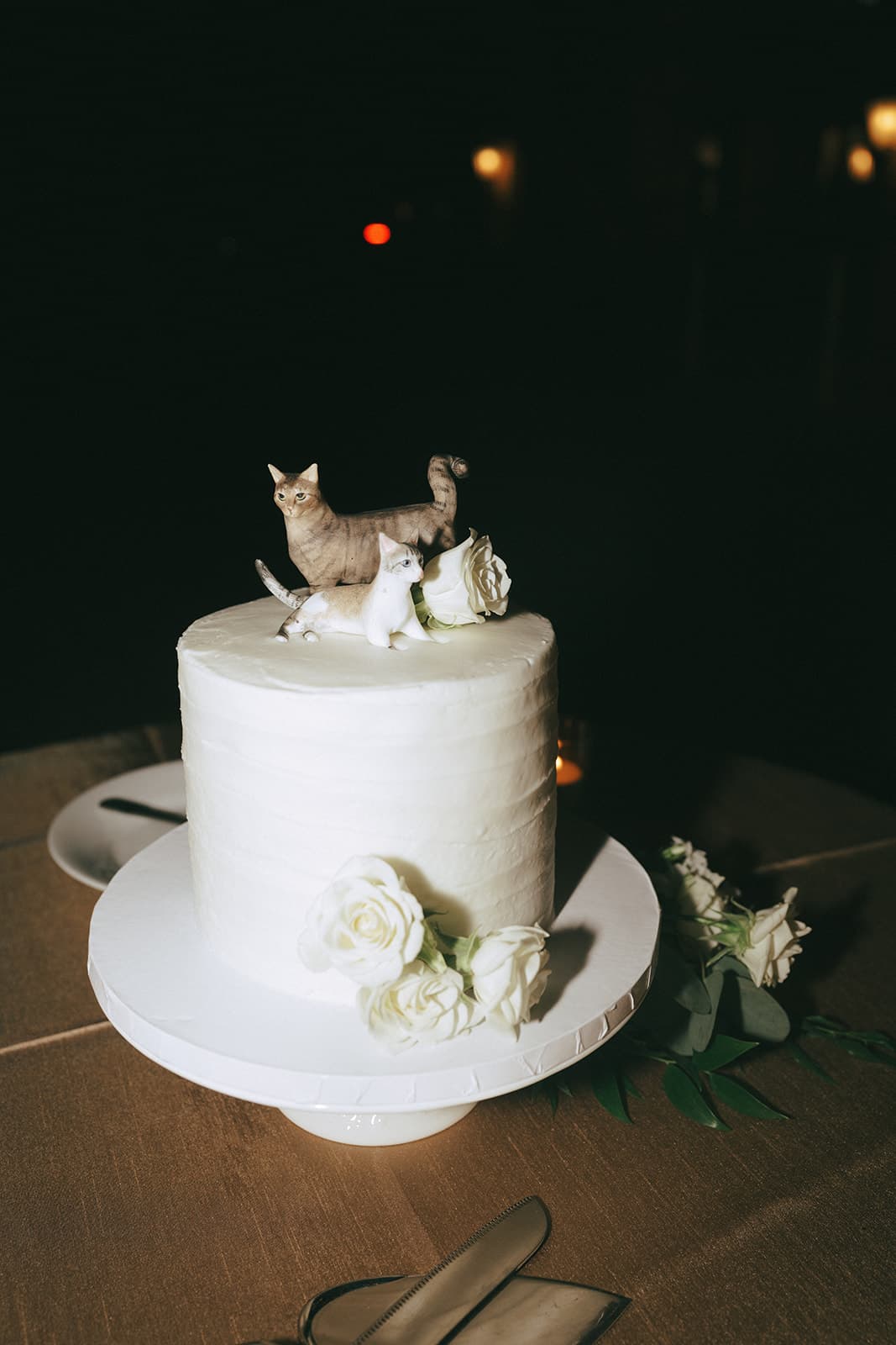 A white buttercream cake topped with two cat figurines and white roses