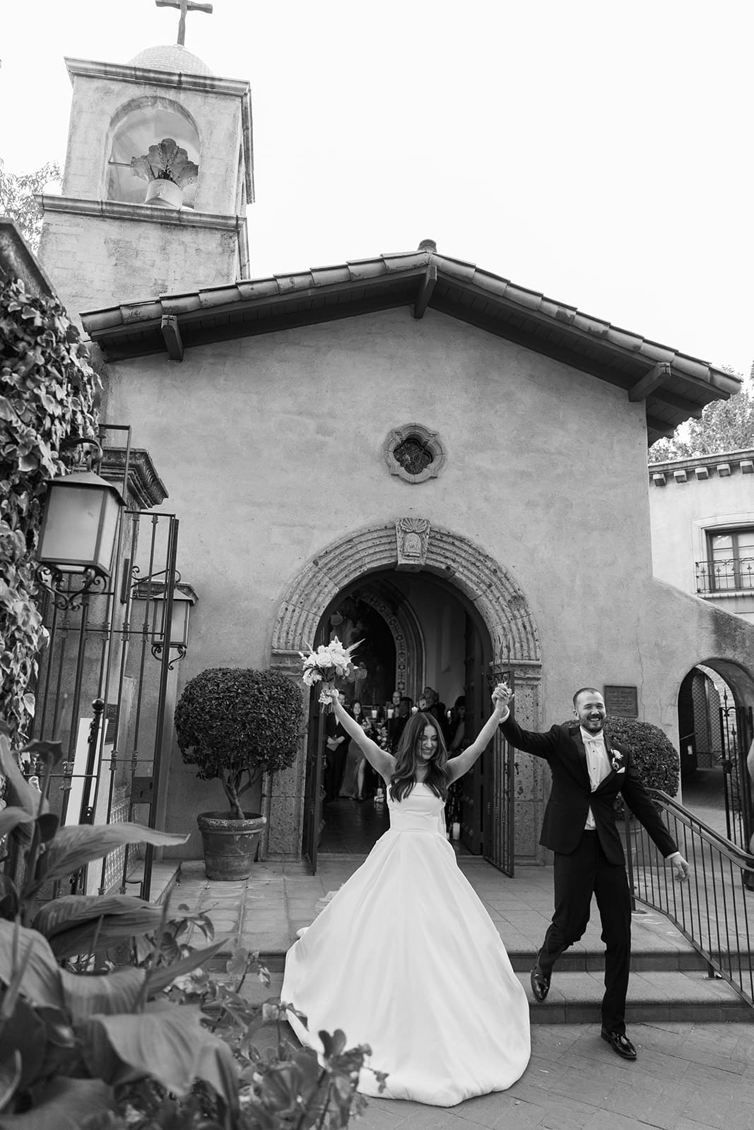Abby and Connor walking out of the chapel with arms raised, in black and white
