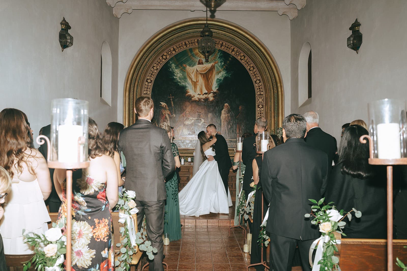 The first kiss at the altar of the Tlaquepaque chapel, guests standing between candlelit pews