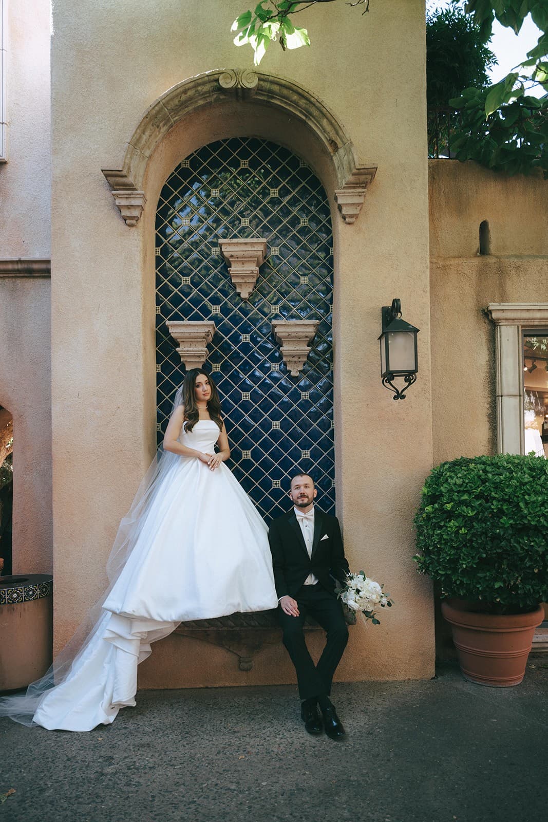 Abby and Connor holding hands before the blue-tiled niche at Tlaquepaque, her cathedral veil pooling at her feet