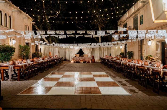 A warm-toned checkerboard dance floor in the center of the courtyard with banquet tables on either side