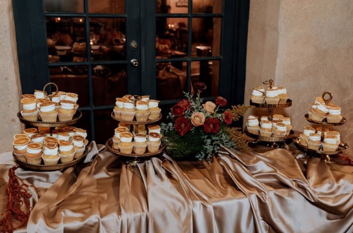A dessert table of tiered cupcake stands and florals on satin draping