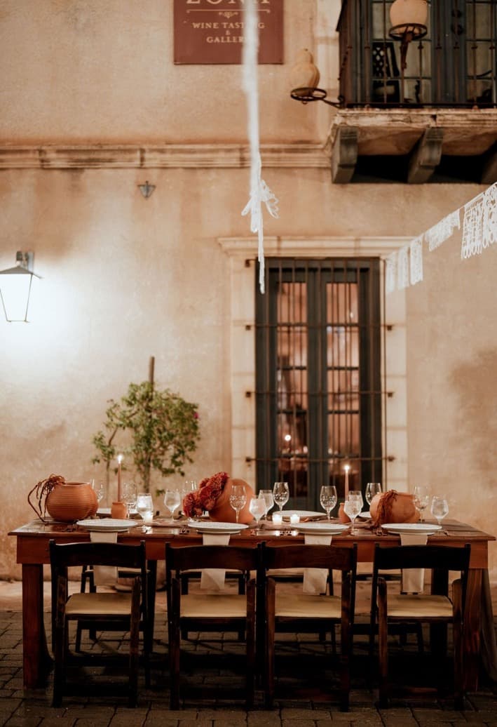 A candlelit banquet table with terracotta vessels against a Tlaquepaque wall at night
