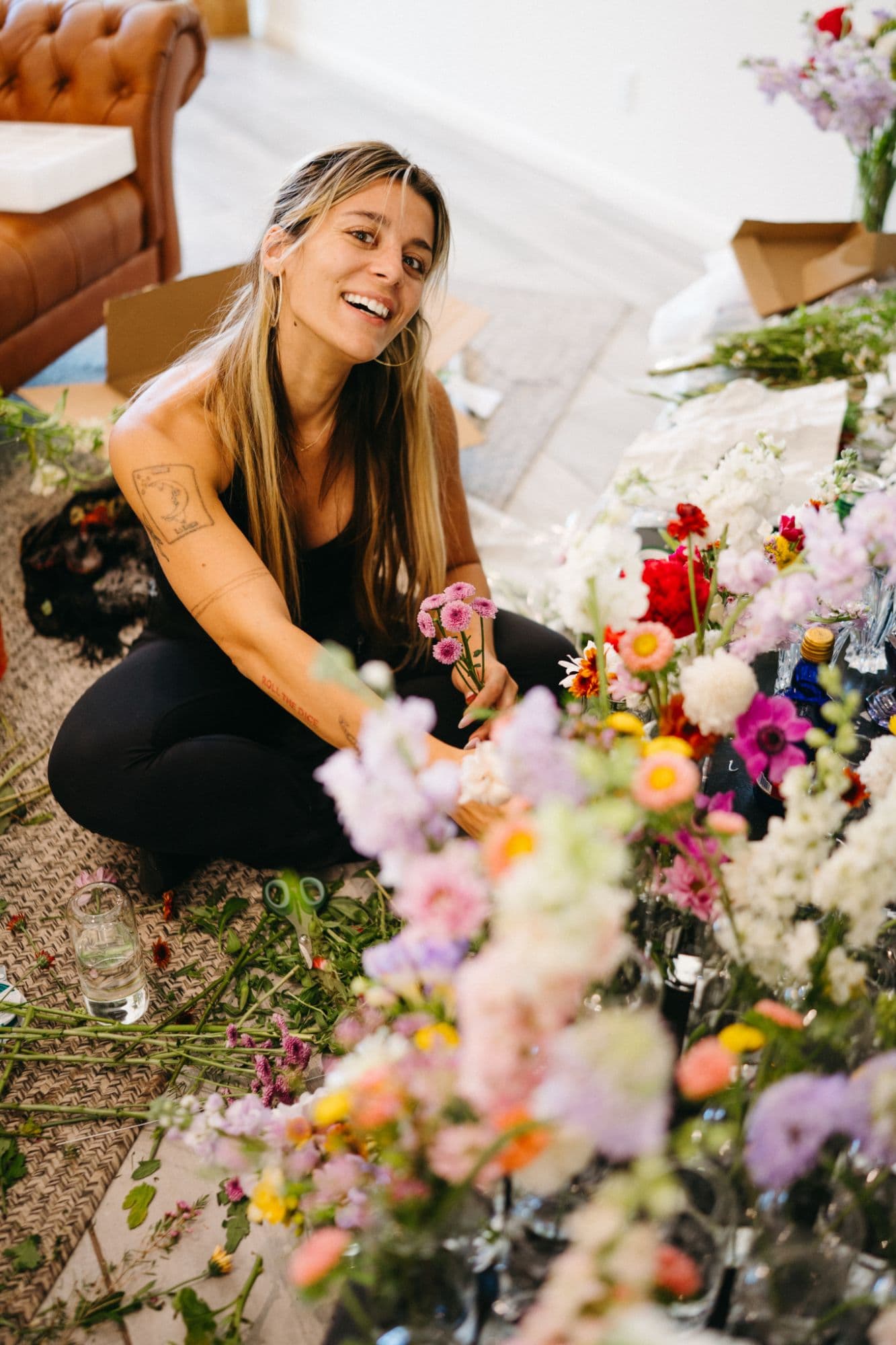 Arabella smiling on the floor surrounded by wildflower arrangements in progress