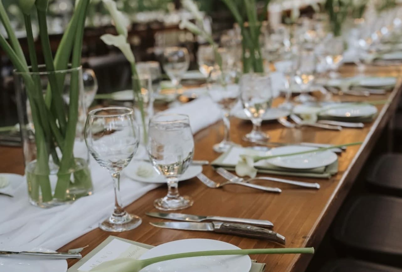 Calla lilies in tall glass vases and a calla laid across each plate on a long wooden table with chiffon runners