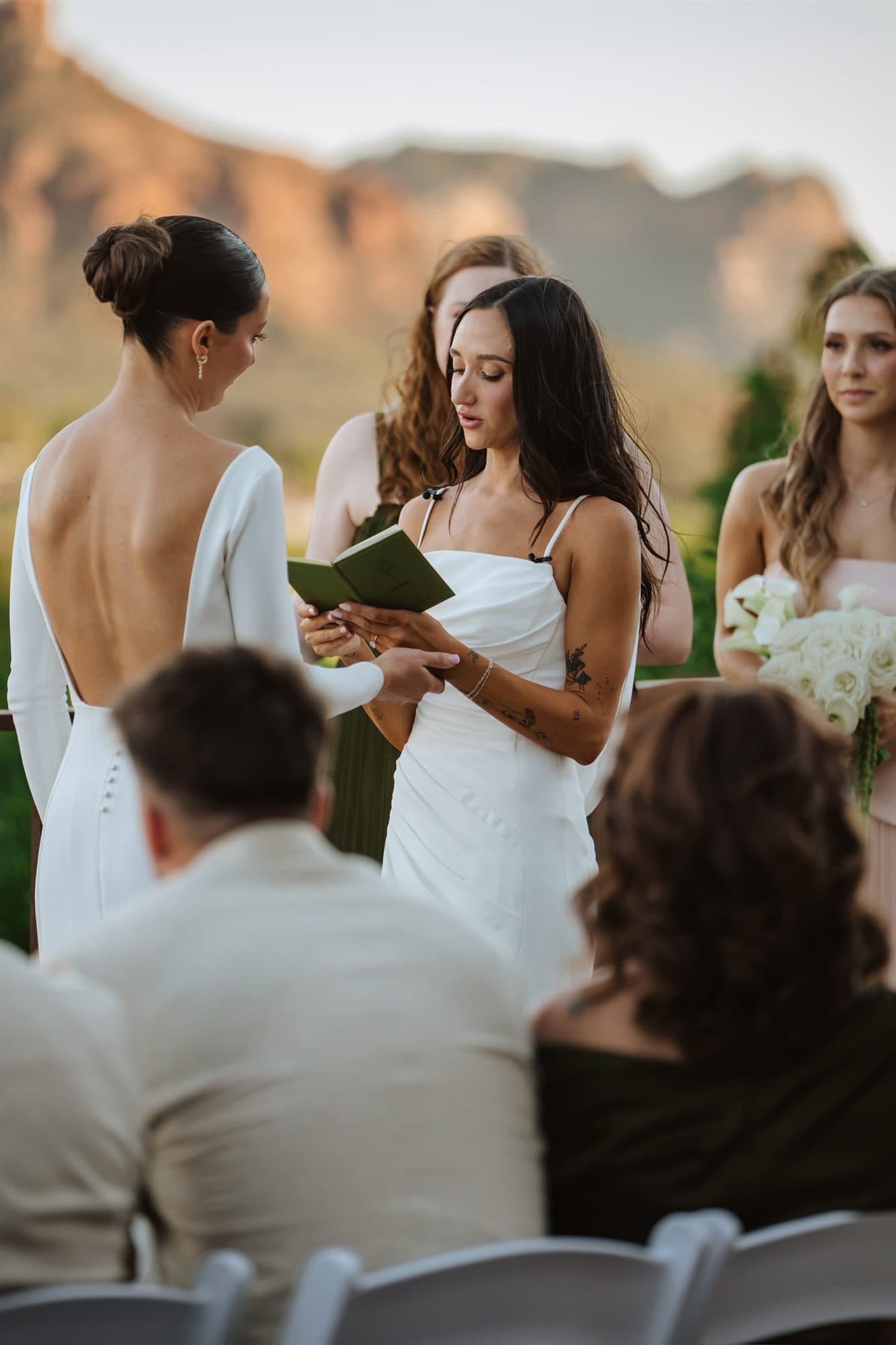 Reading vows from a small green book as the wedding party looks on