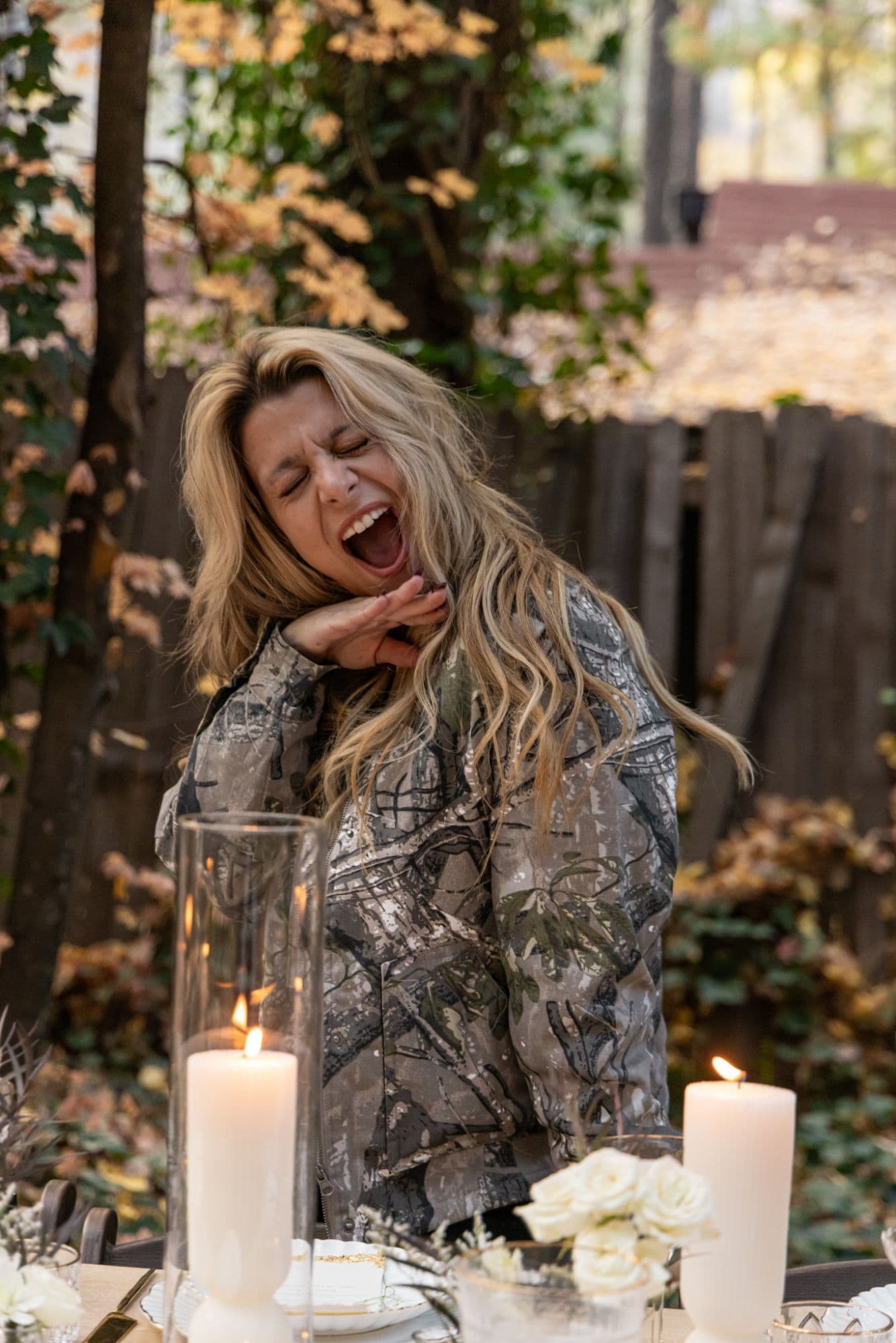 A candid laugh behind the candles and white roses of a forest tablescape