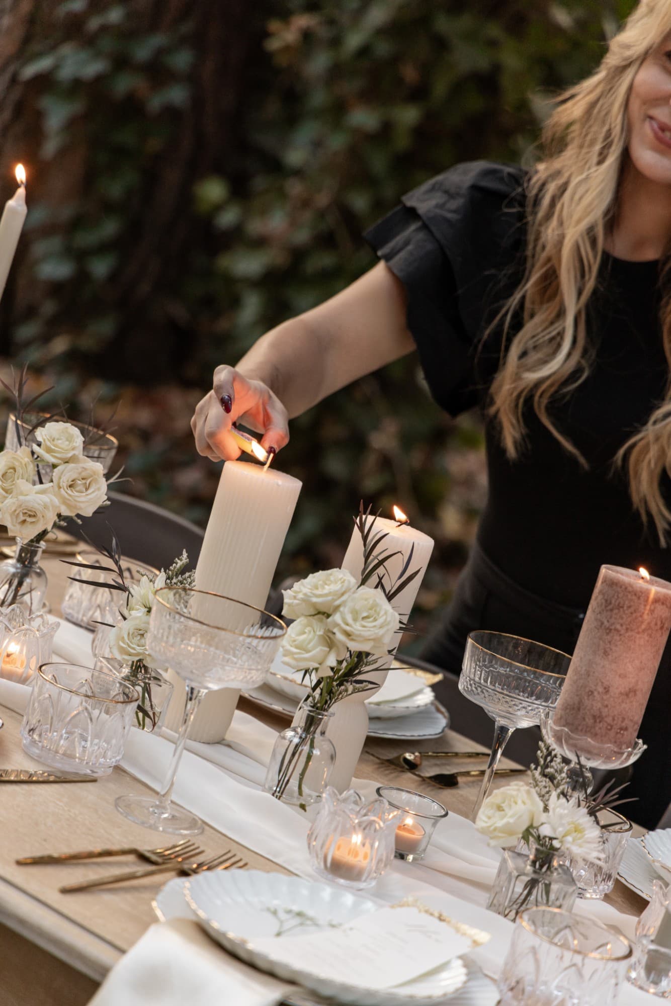 Lighting a ribbed pillar candle among white roses and gold-rimmed coupes