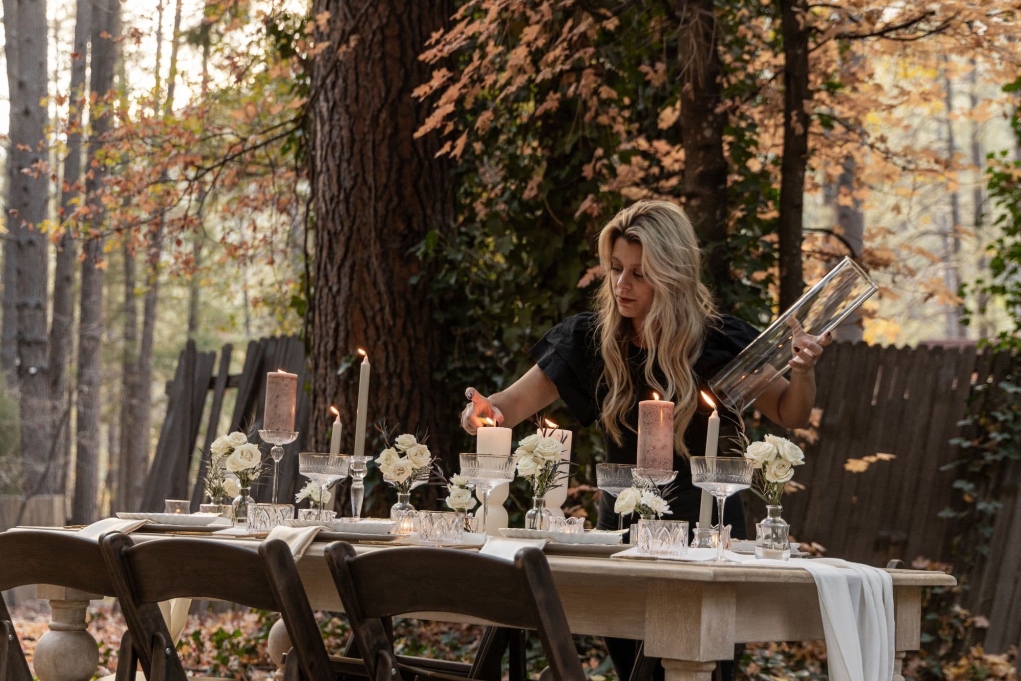 Lighting the pillar candles on a long forest tablescape beneath autumn trees