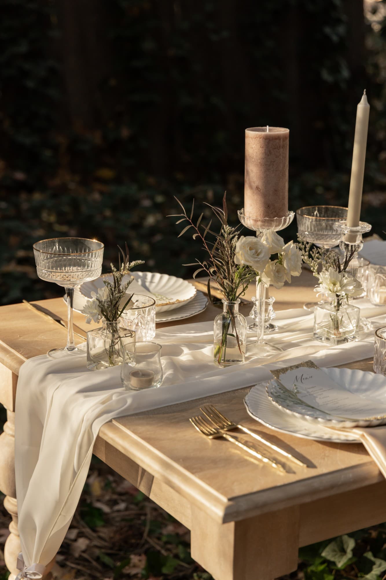 Mauve pillar and ivory taper candles with white roses in bud vases on a chiffon runner