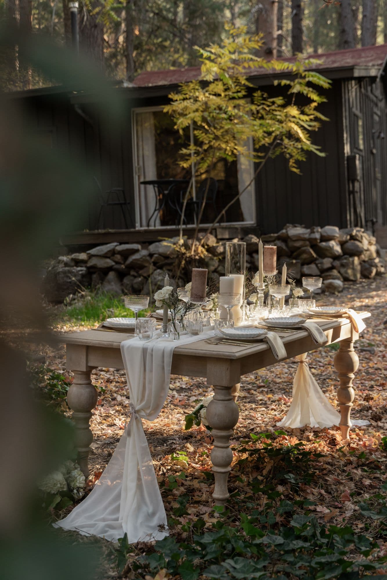 A long candlelit table set beneath towering pines