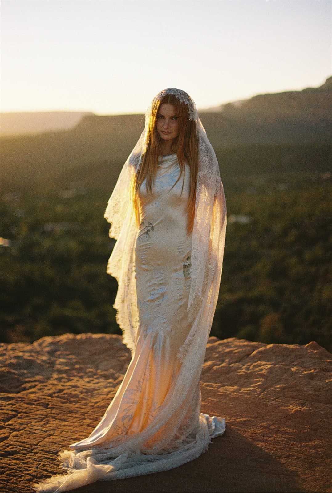 A bride in a lace veil glowing at sunset above the Sedona red rocks