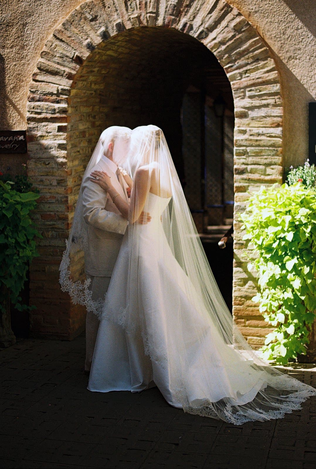 A bride in a cathedral veil beneath a stone archway, on 35mm film