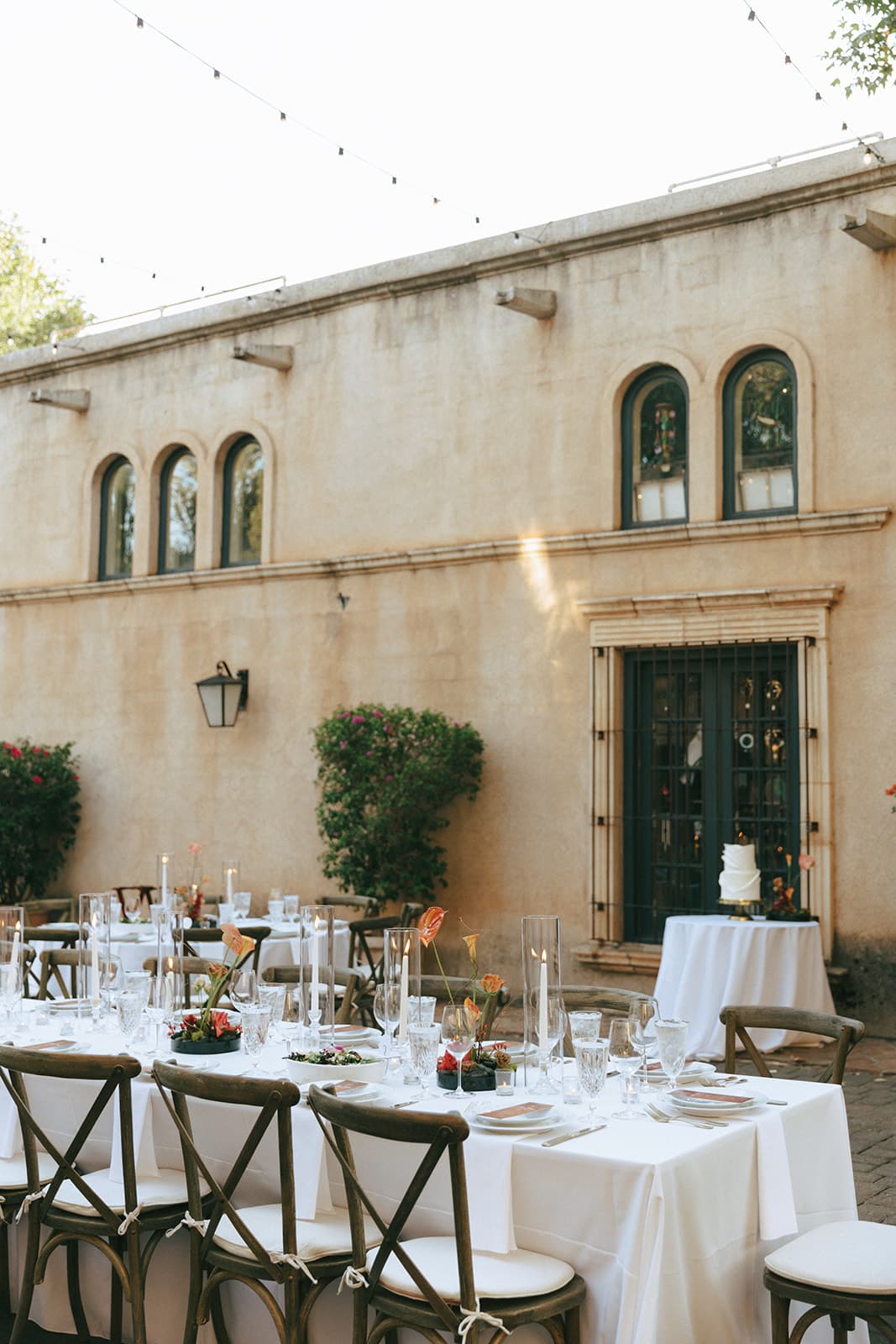 Tables beneath arched windows with the white wedding cake in the background