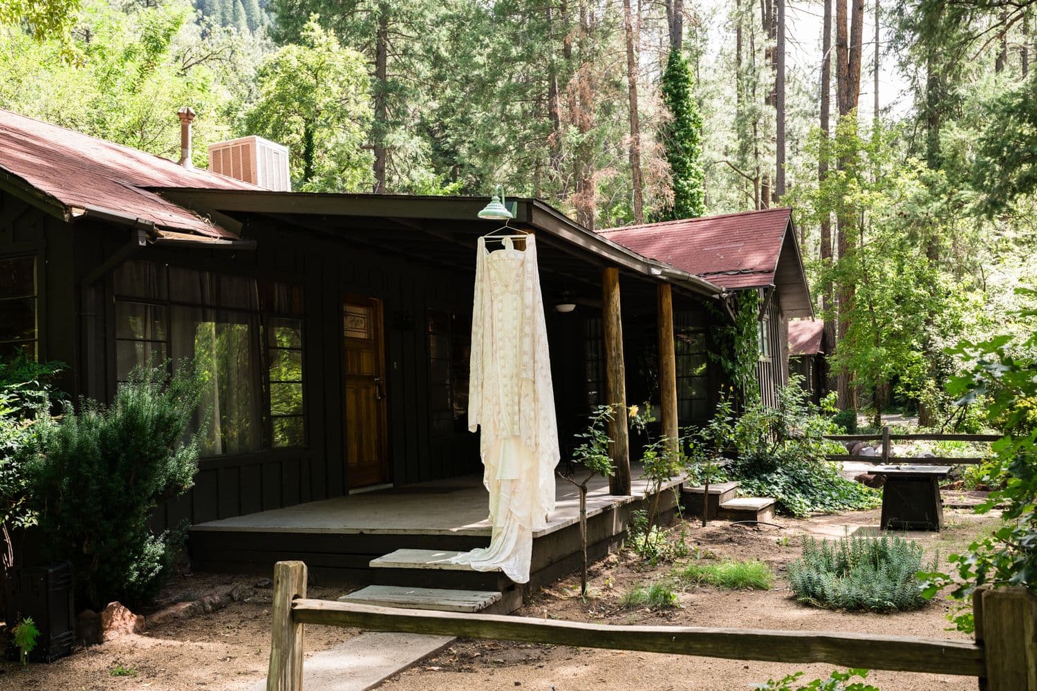 The bride's caped lace gown hanging from the porch of a forest cabin at Don Hoel's