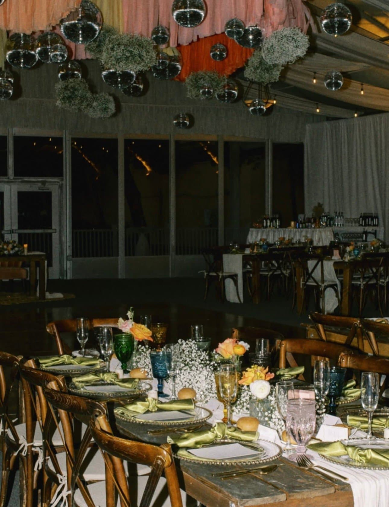Disco balls and baby's breath clouds suspended above long tables set with colored vintage glassware and green satin napkins
