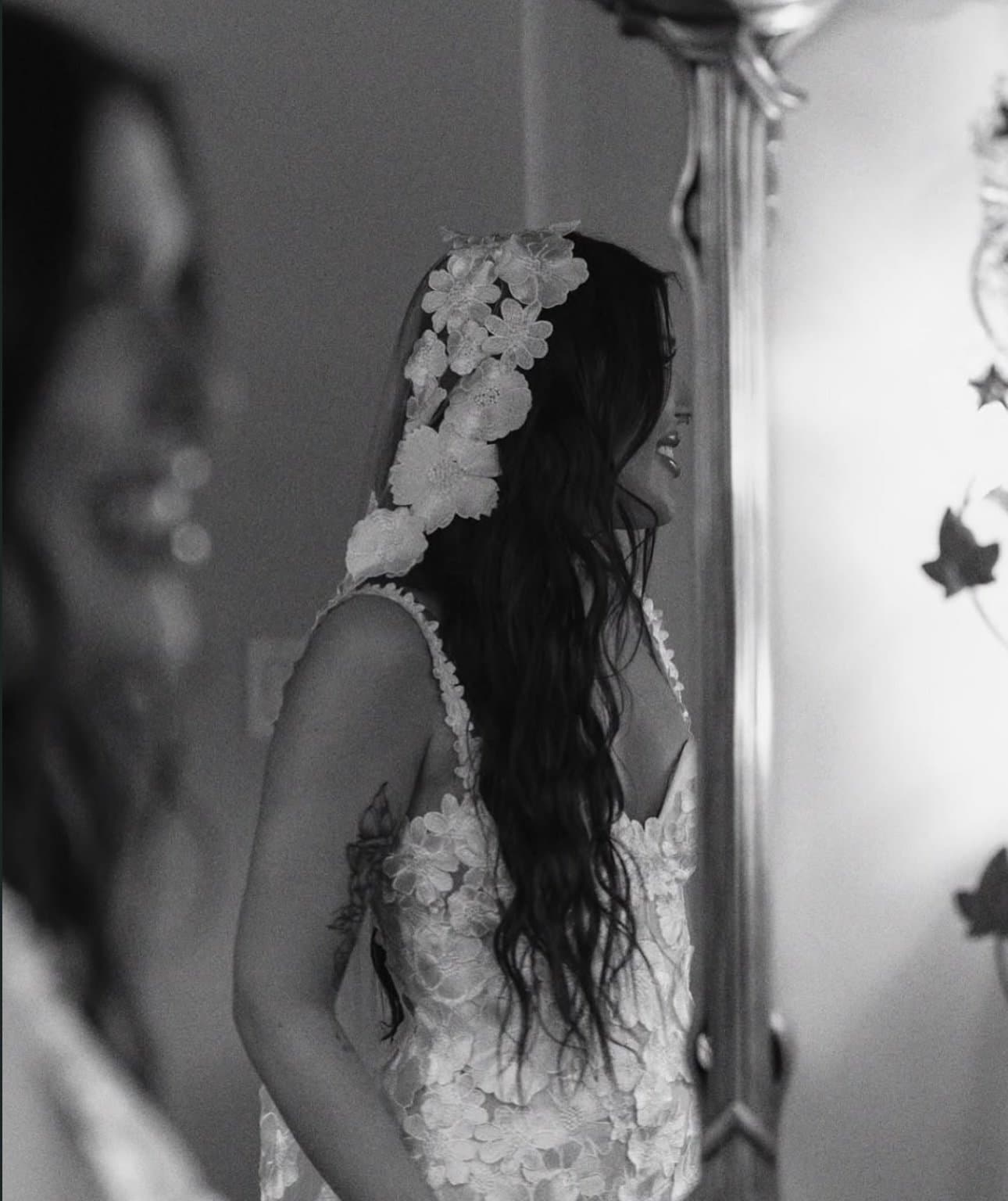 Isa in her dimensional floral veil and gown, reflected in a gilded mirror, in black and white