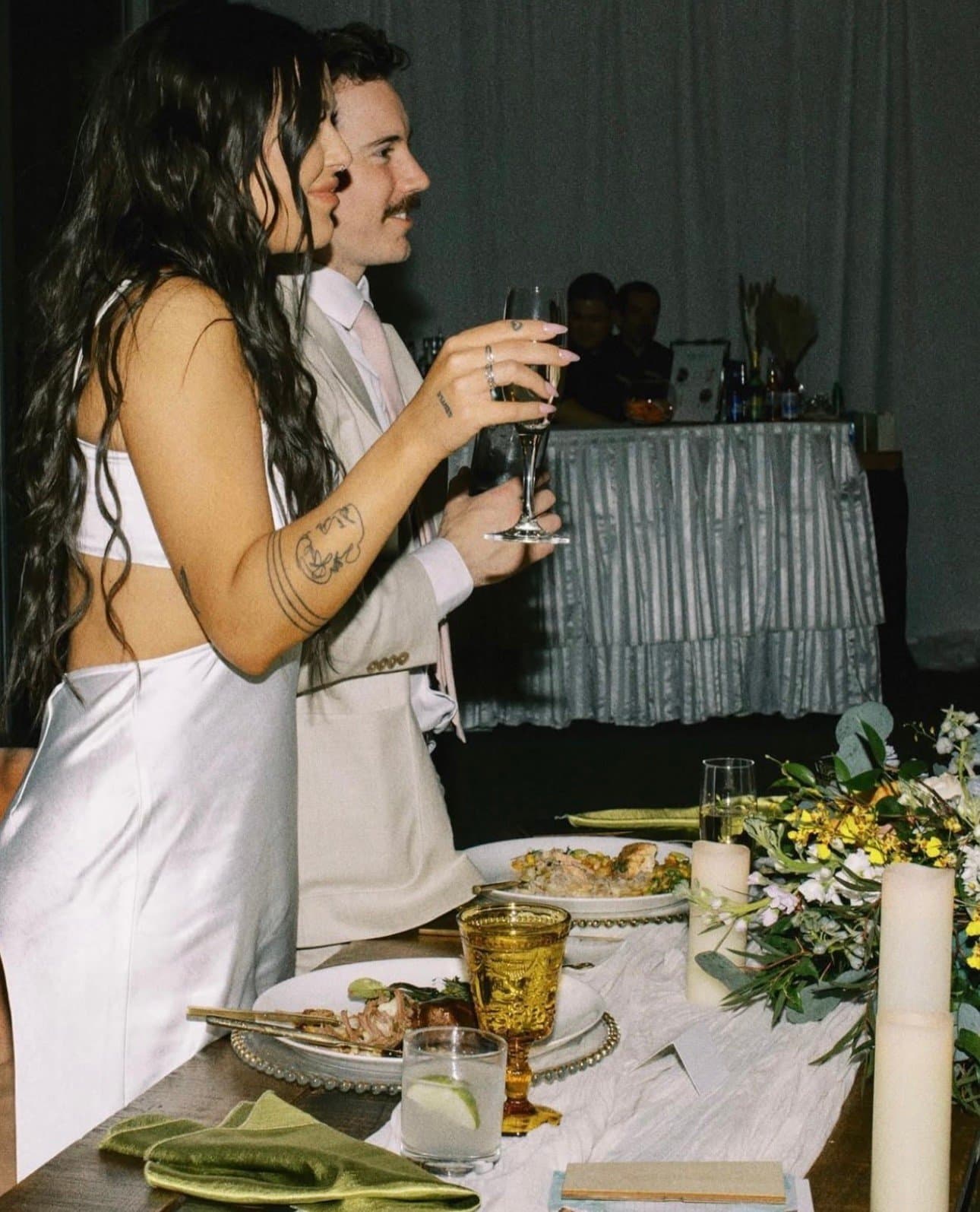 Isa and Dylan raising a toast at their sweetheart table beside an amber goblet and garden florals