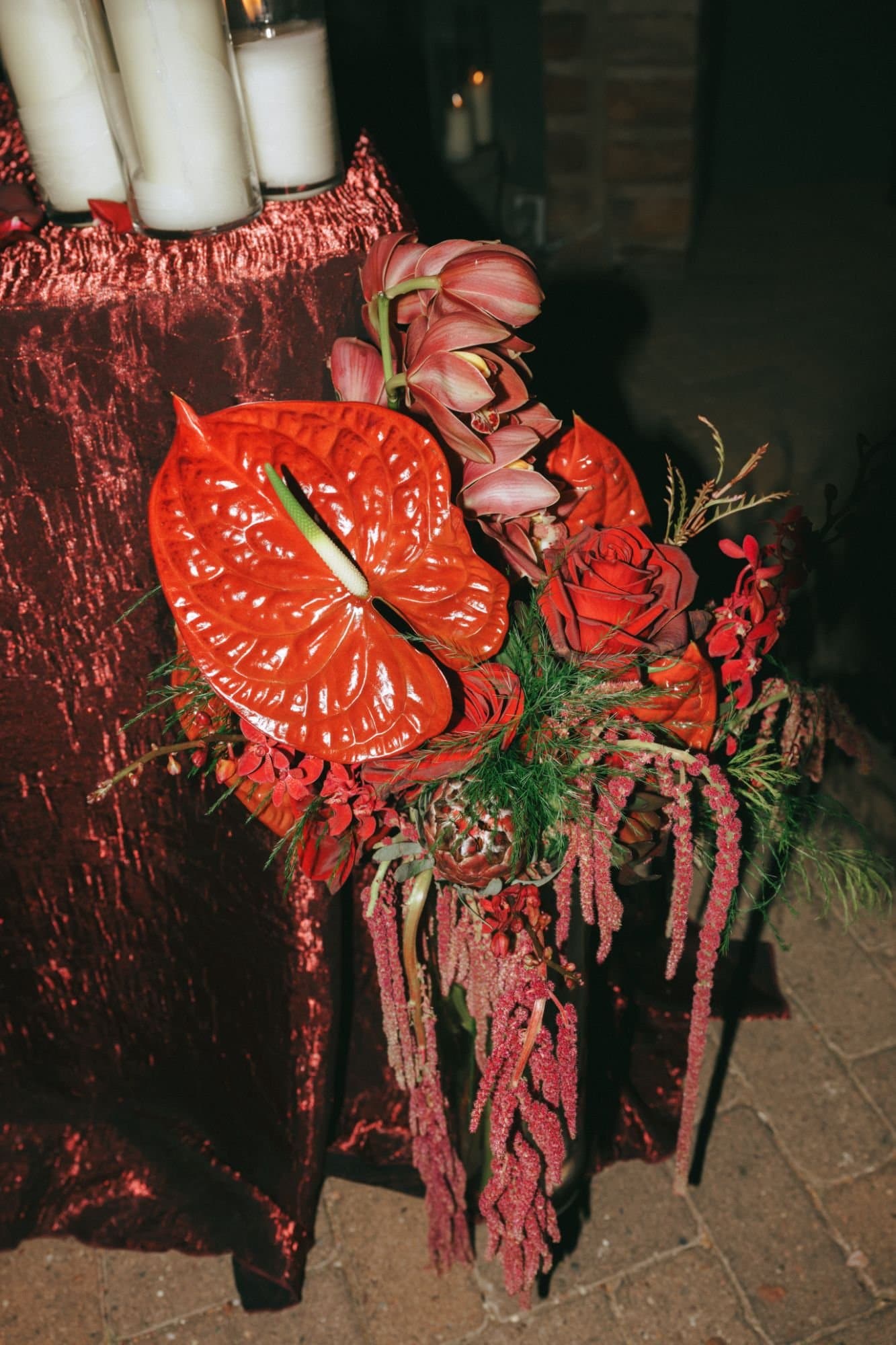 Red anthurium, cymbidium orchids, roses and cascading amaranthus against a red sequined linen