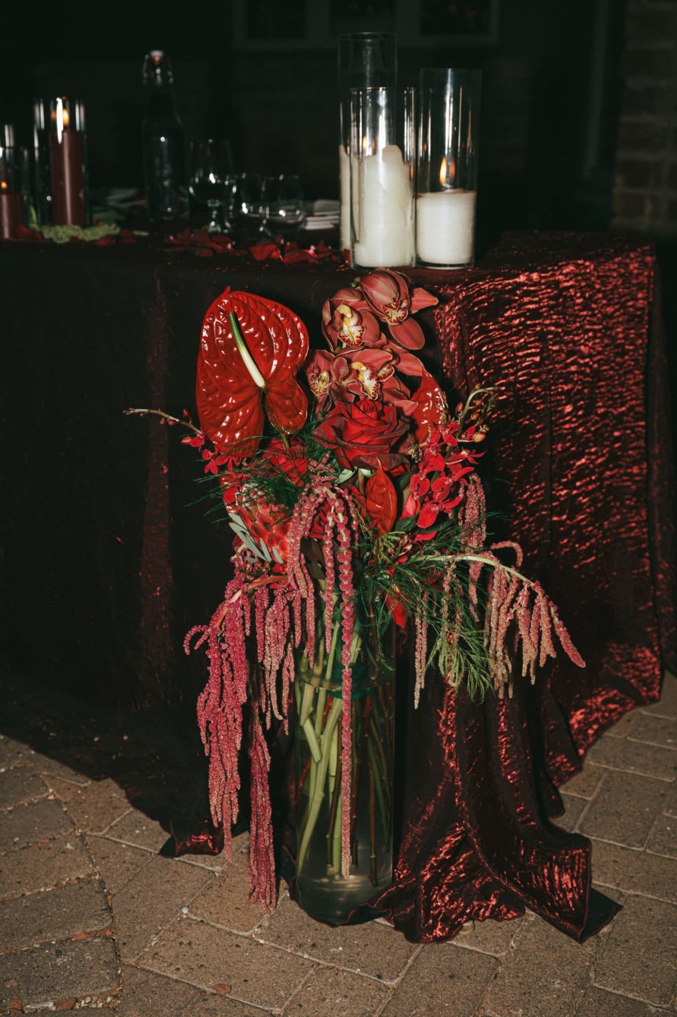 A floor arrangement of red florals and amaranthus beside the sweetheart table's red sequined linen and pillar candles