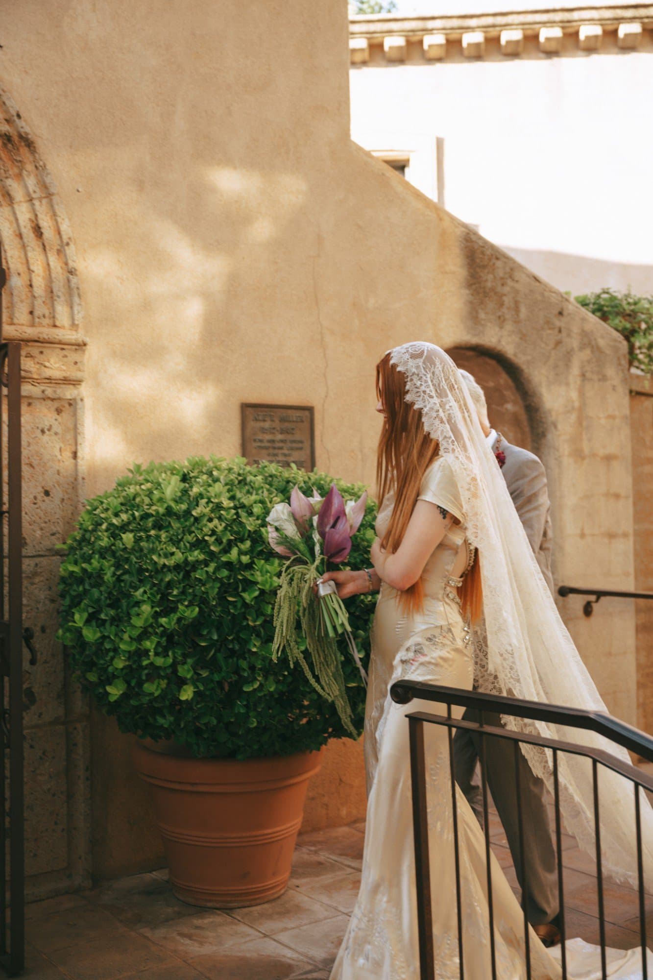 Walking to the chapel past a terracotta planter, the lace veil trailing behind
