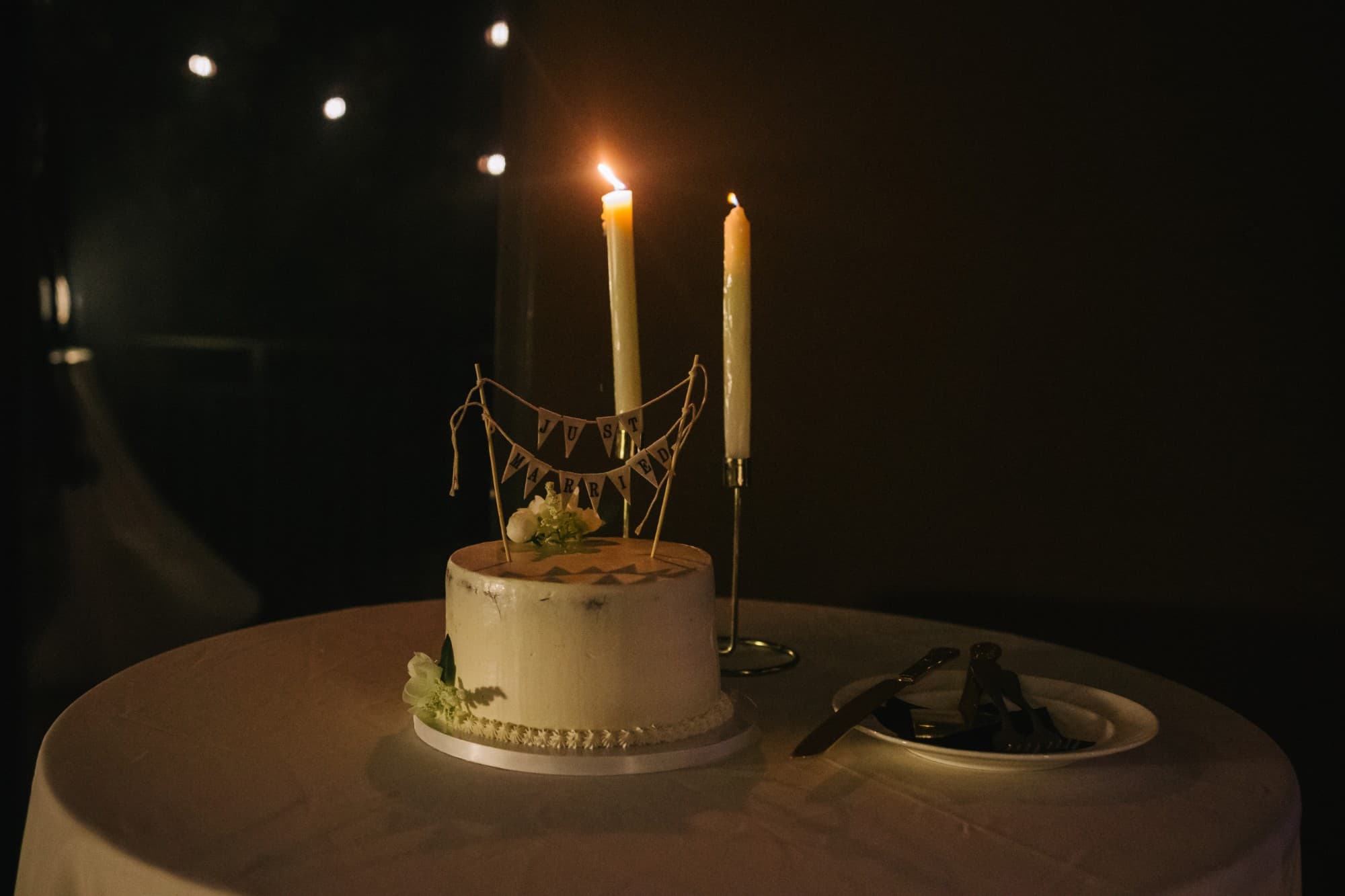 A single-tier cake with a Just Married banner by candlelight