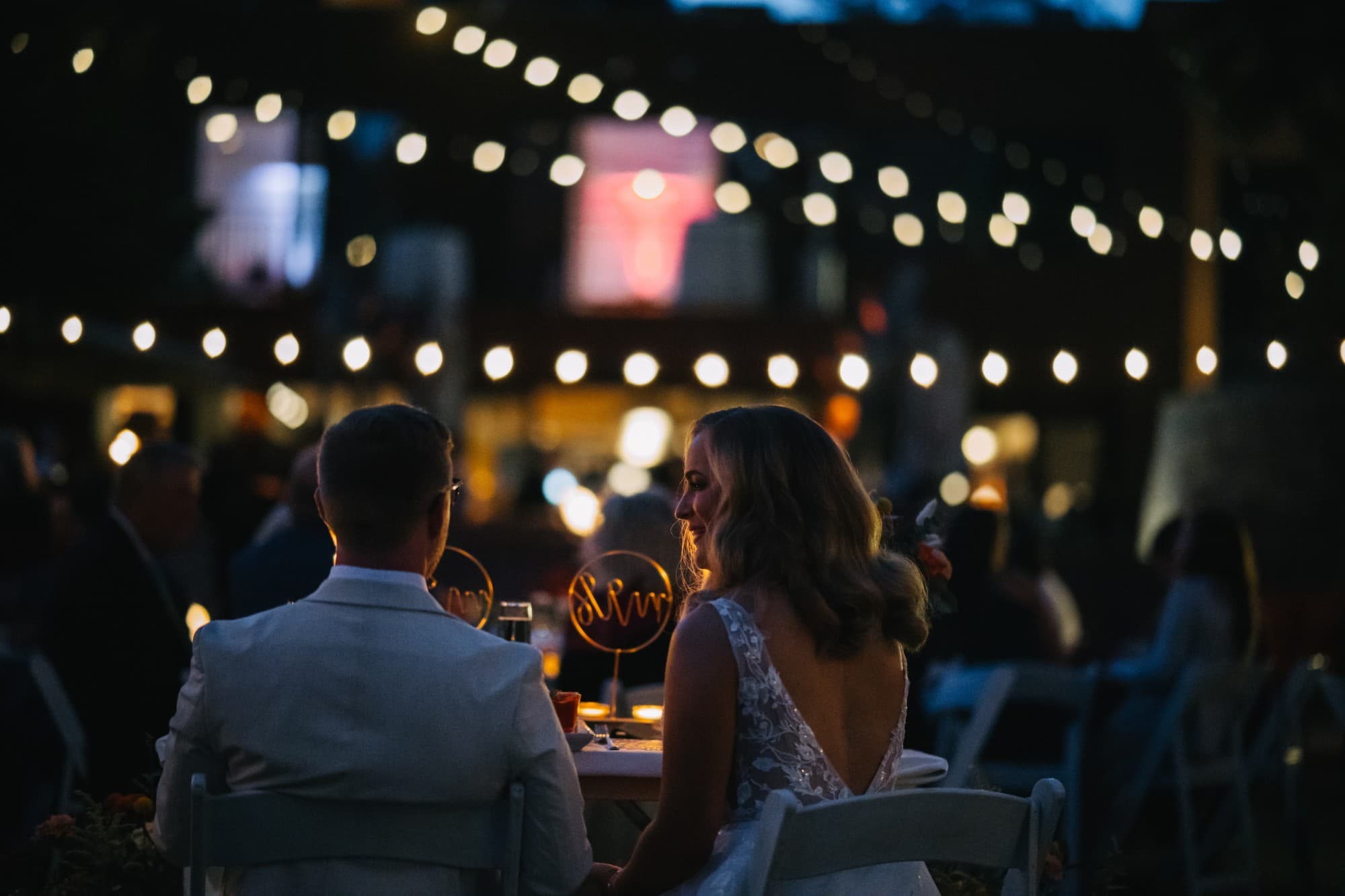 Jenna and Derek at the sweetheart table beneath glowing string lights