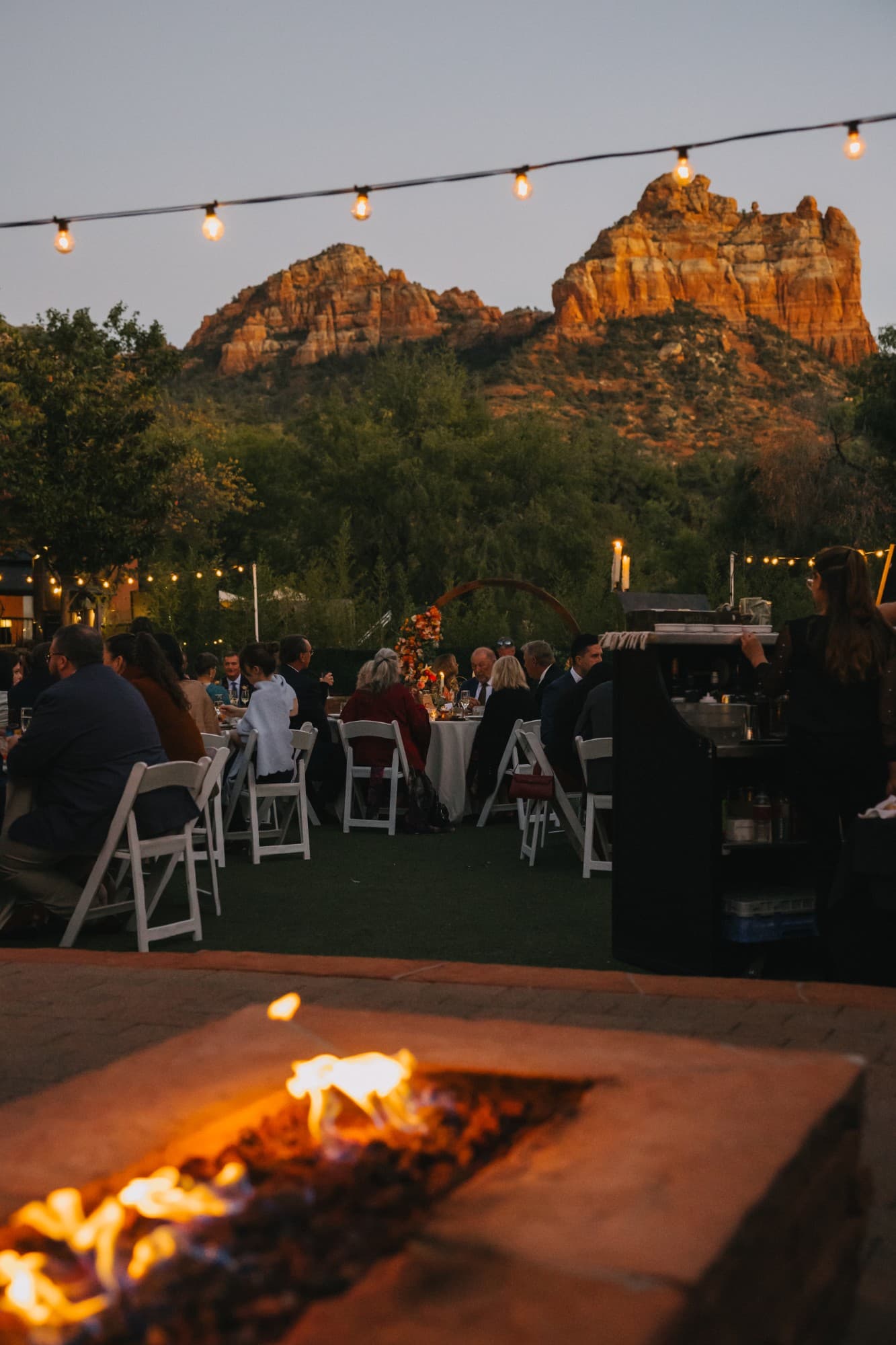 The reception beneath string lights at dusk, the red rocks glowing beyond a fire pit