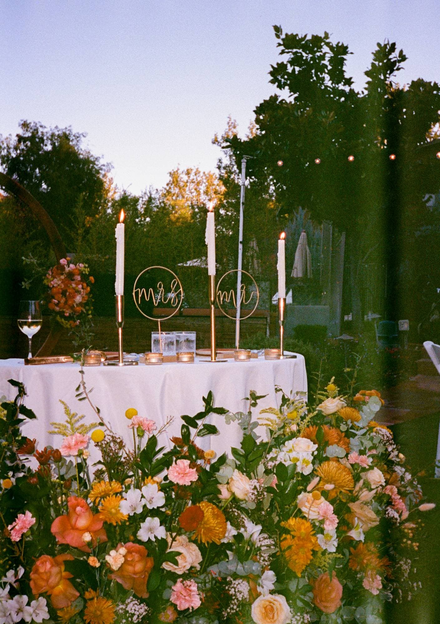 The sweetheart table with gold Mr. and Mrs. signs, taper candles and a bank of colorful florals, on film