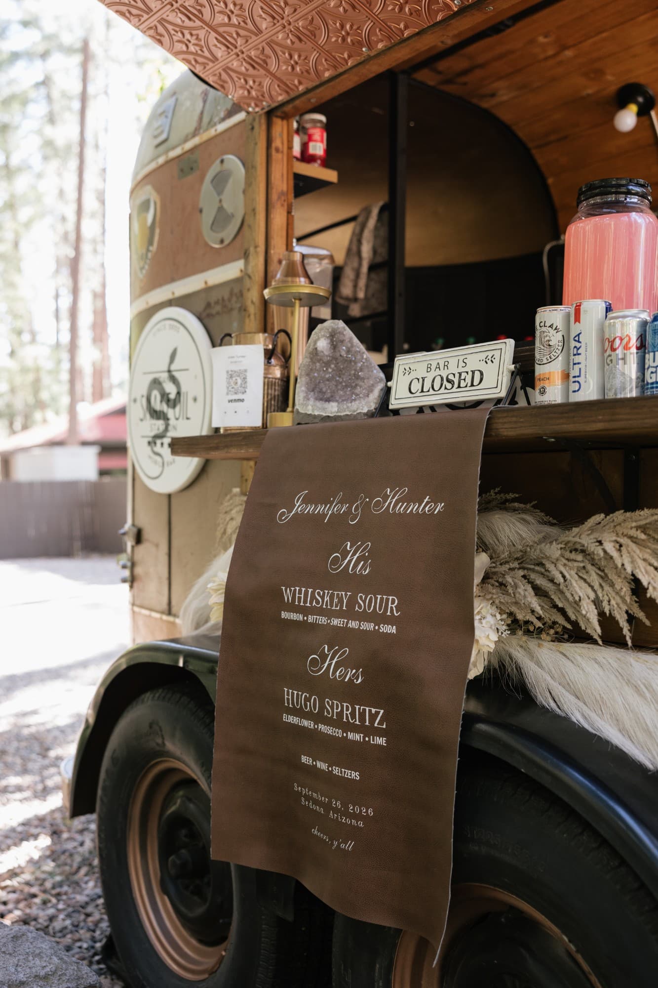 A vintage horse-trailer bar with a leather signature drinks sign, crystals and pampas grass