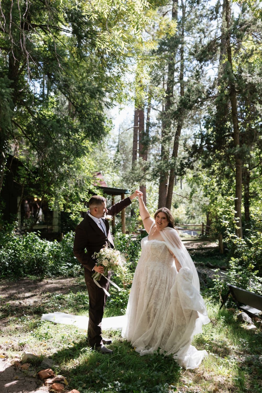 The groom twirling the bride beneath tall pines beside the cabins at Don Hoel’s
