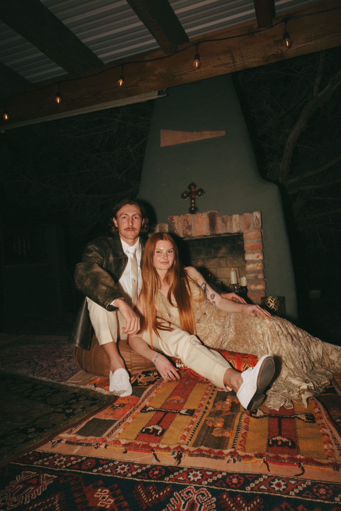 Newlyweds lounging on layered vintage rugs in front of a kiva fireplace