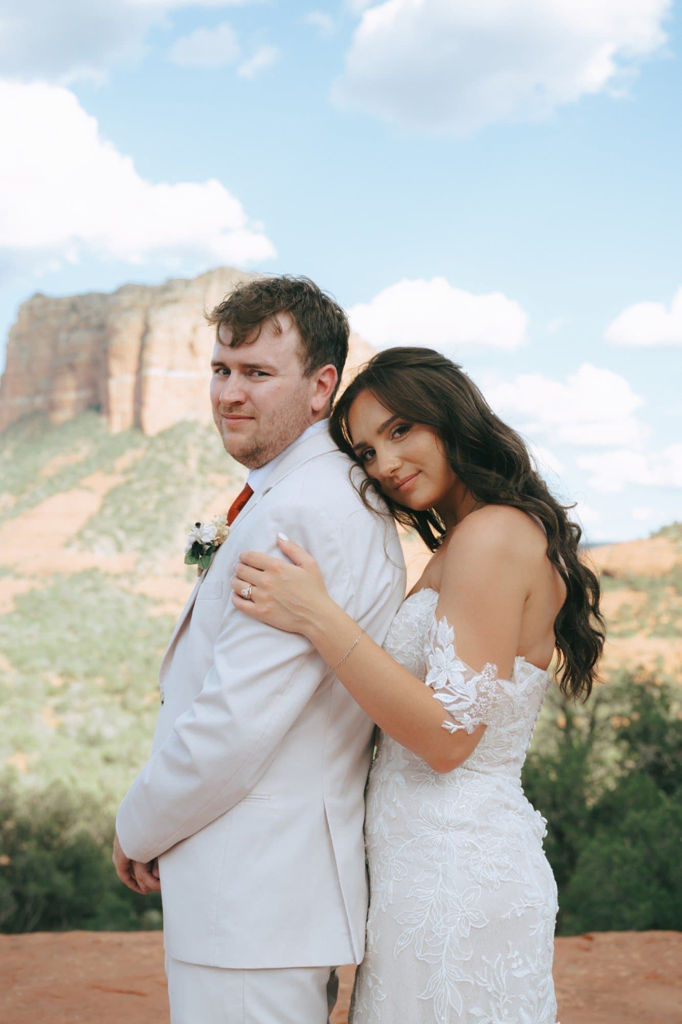 A bride resting her head on her groom’s shoulder before a red rock butte