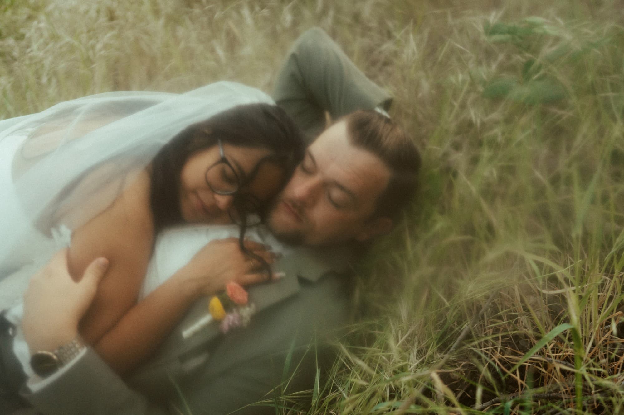 Patricia and Drew lying together in the meadow grass, her veil spread around them