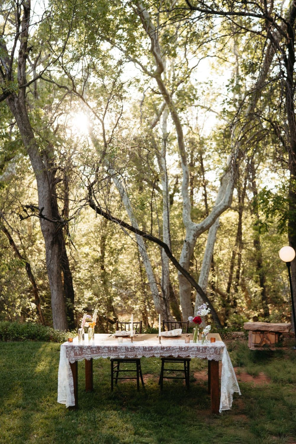 The sweetheart table dressed in vintage lace beneath sunlit sycamores