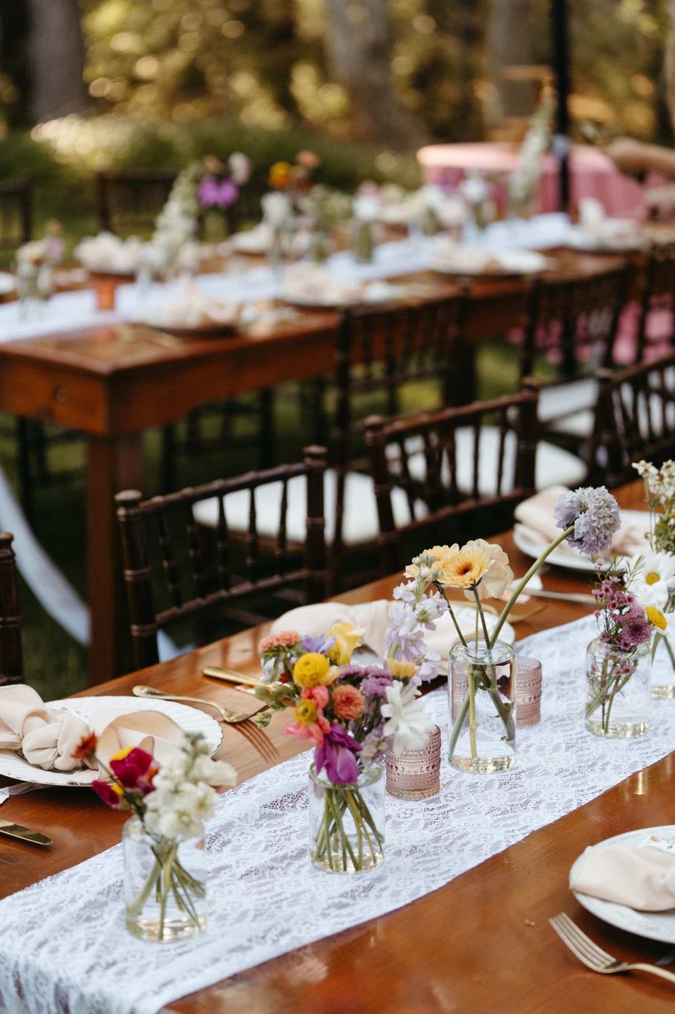 Wildflowers in petite glass vases on a lace runner, with blush napkins and pink glass votives