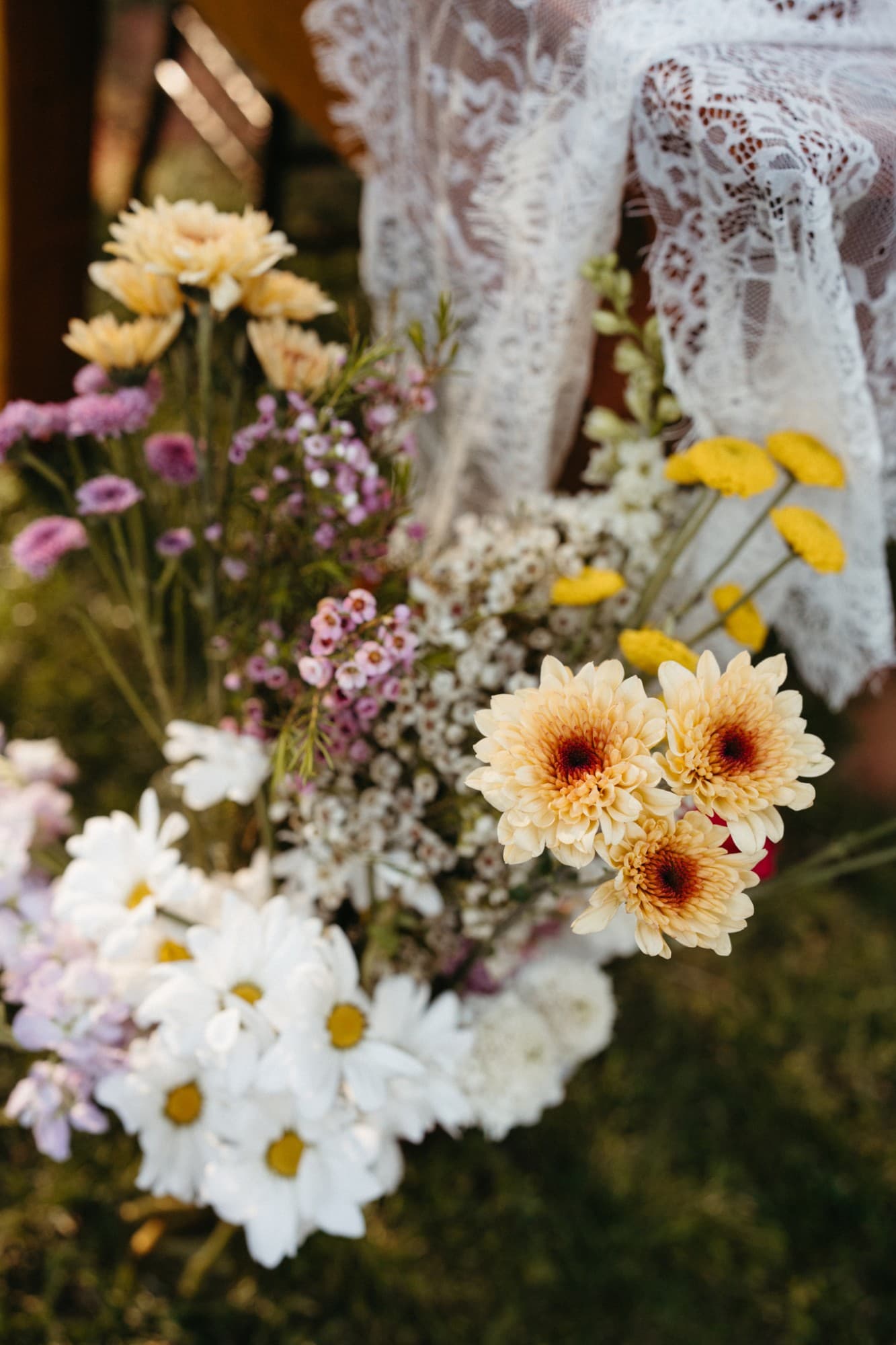 A gathered bunch of daisies, chrysanthemums and waxflower beside a lace overlay
